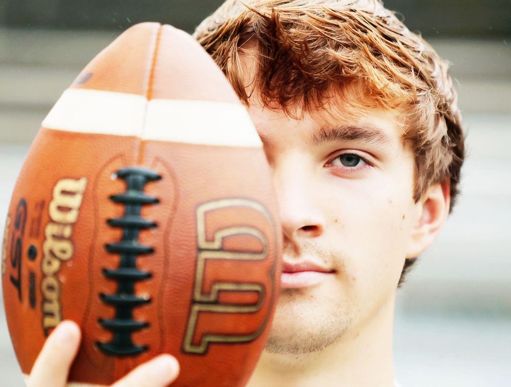 Close-up portrait with football covering half of athlete's face.