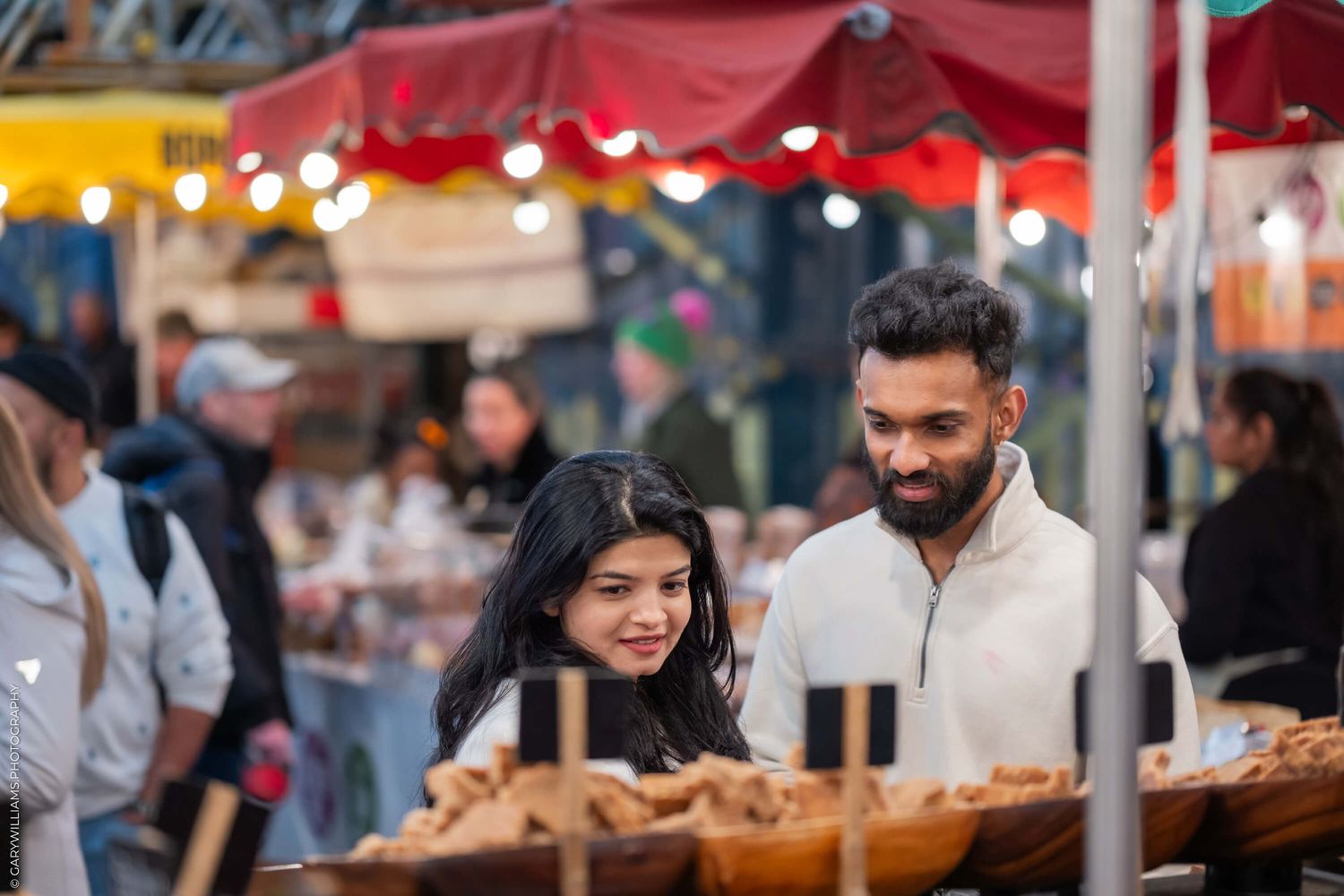 A couple shops at an outdoor market with food stalls.