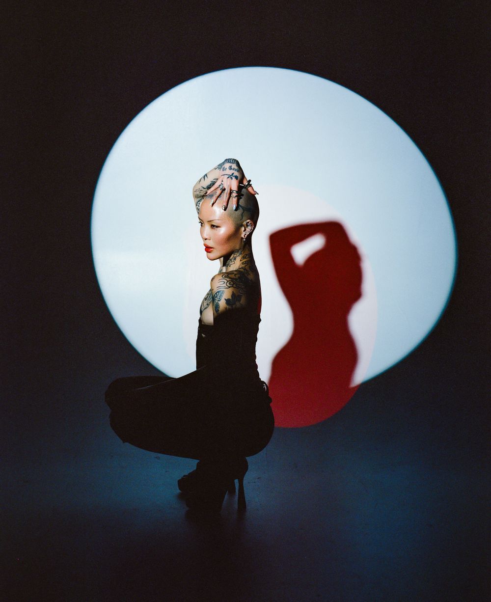 Dramatic silhouette of tattooed model against large circular light with red shadow.