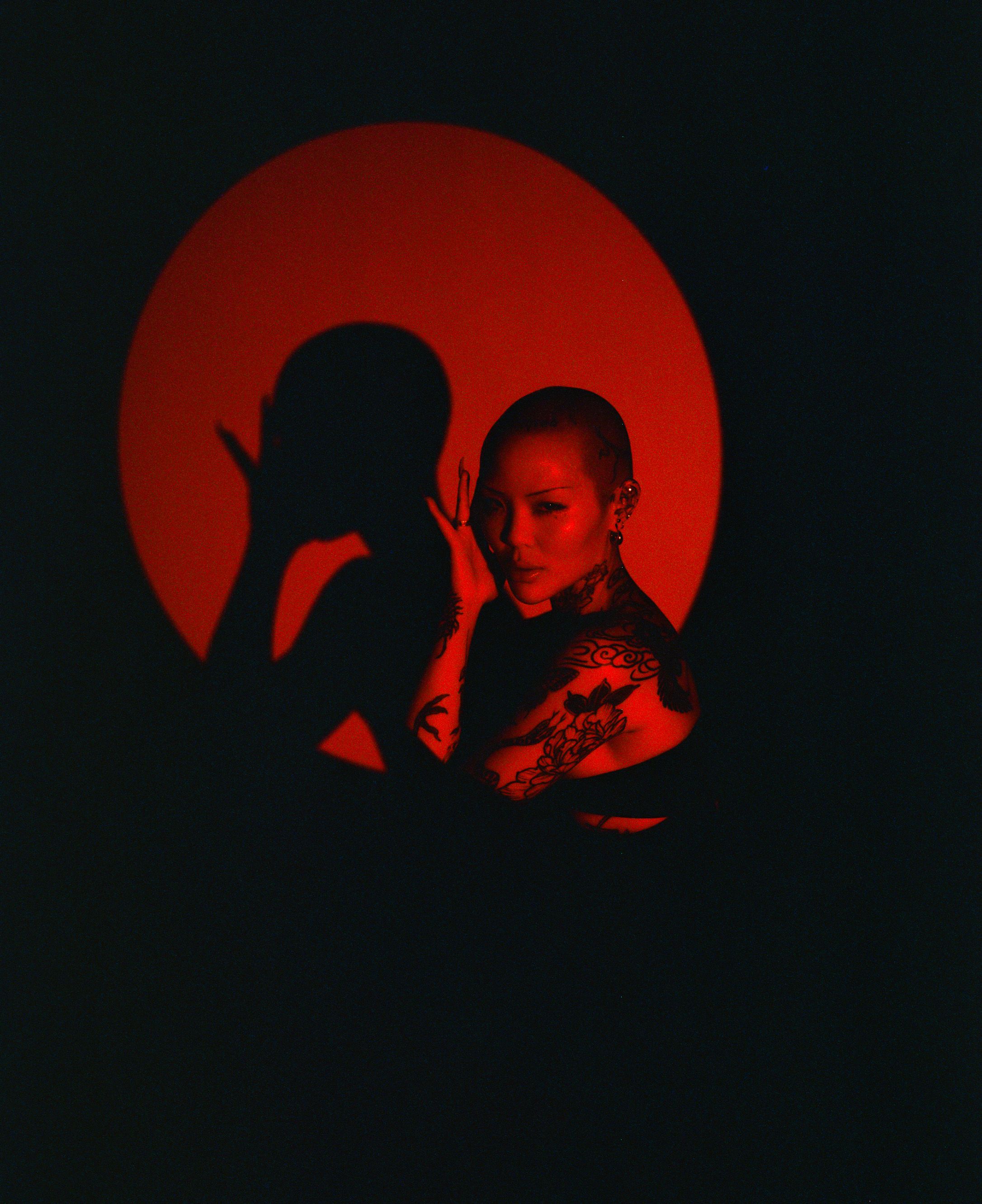 Artistic portrait with red circular backdrop creating dramatic shadow effect.