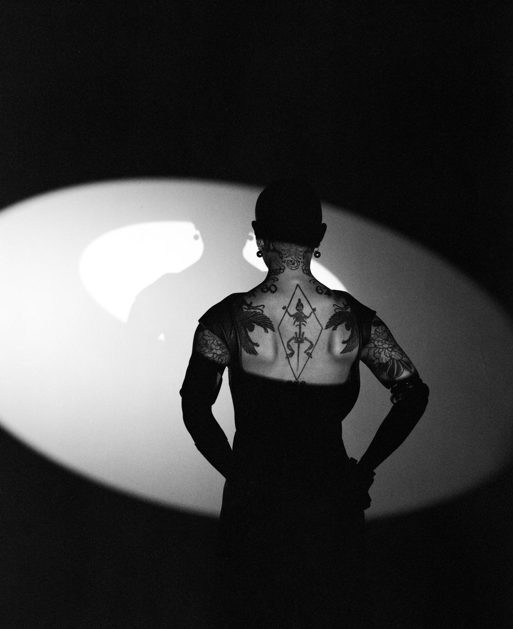 Black and white back portrait showing tattooed shoulders in dramatic spotlight.