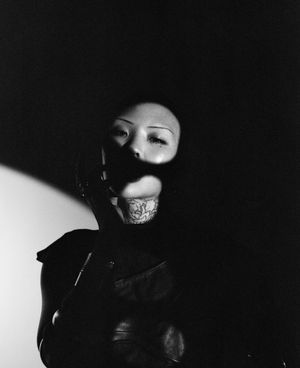 Artistic fashion portrait featuring model in dark attire with dramatic shadow play.