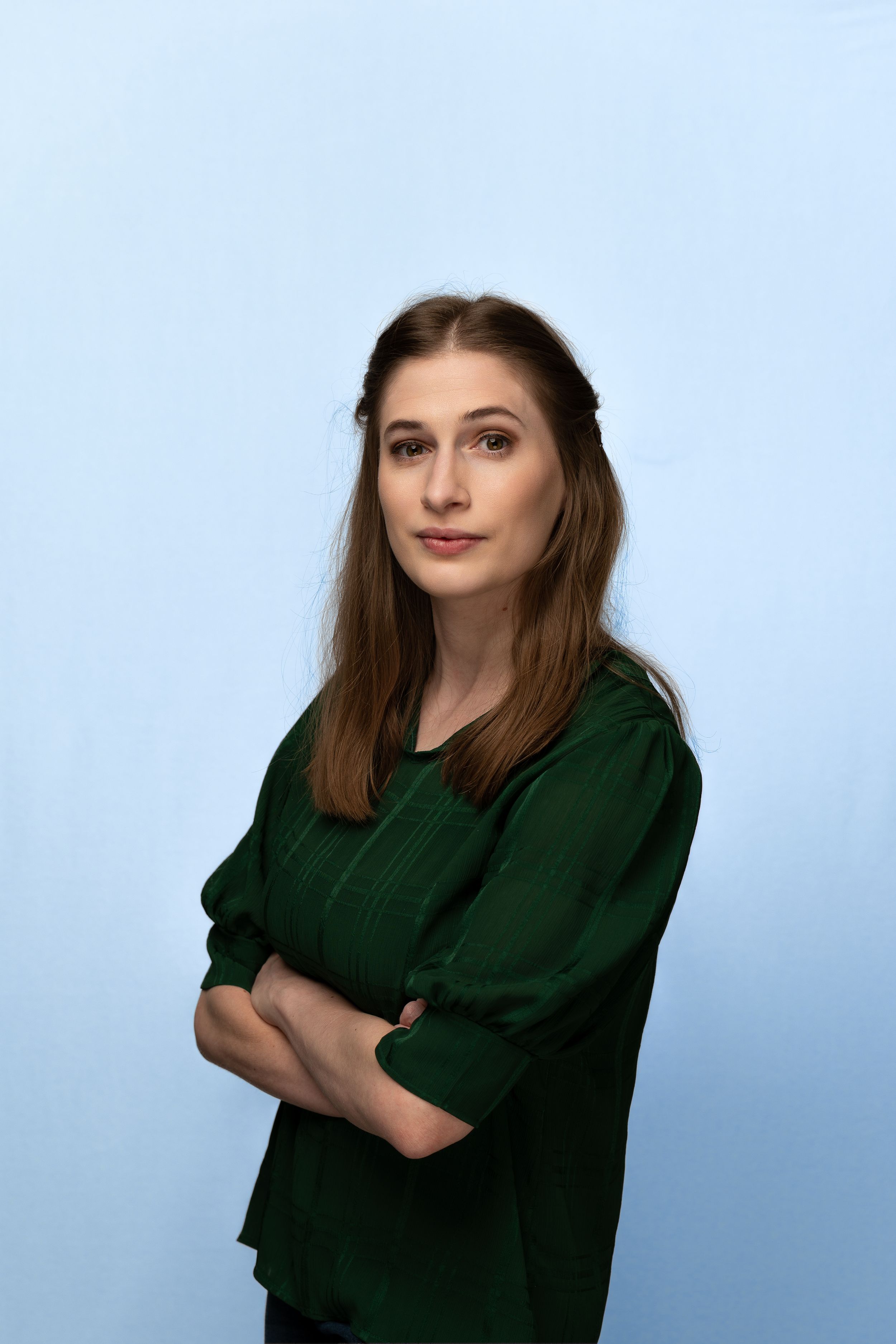 Portrait of person in dark green top against light blue background with arms crossed.