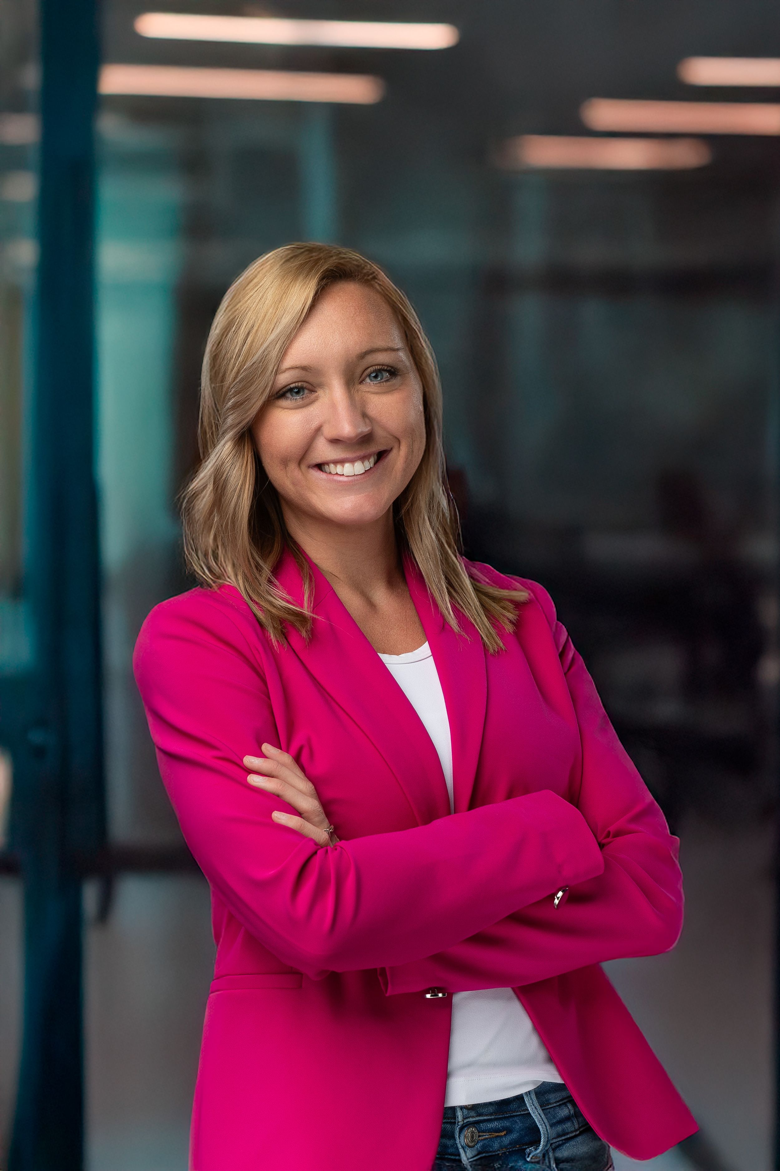 Business portrait of person in pink blazer and white top with crossed arms.