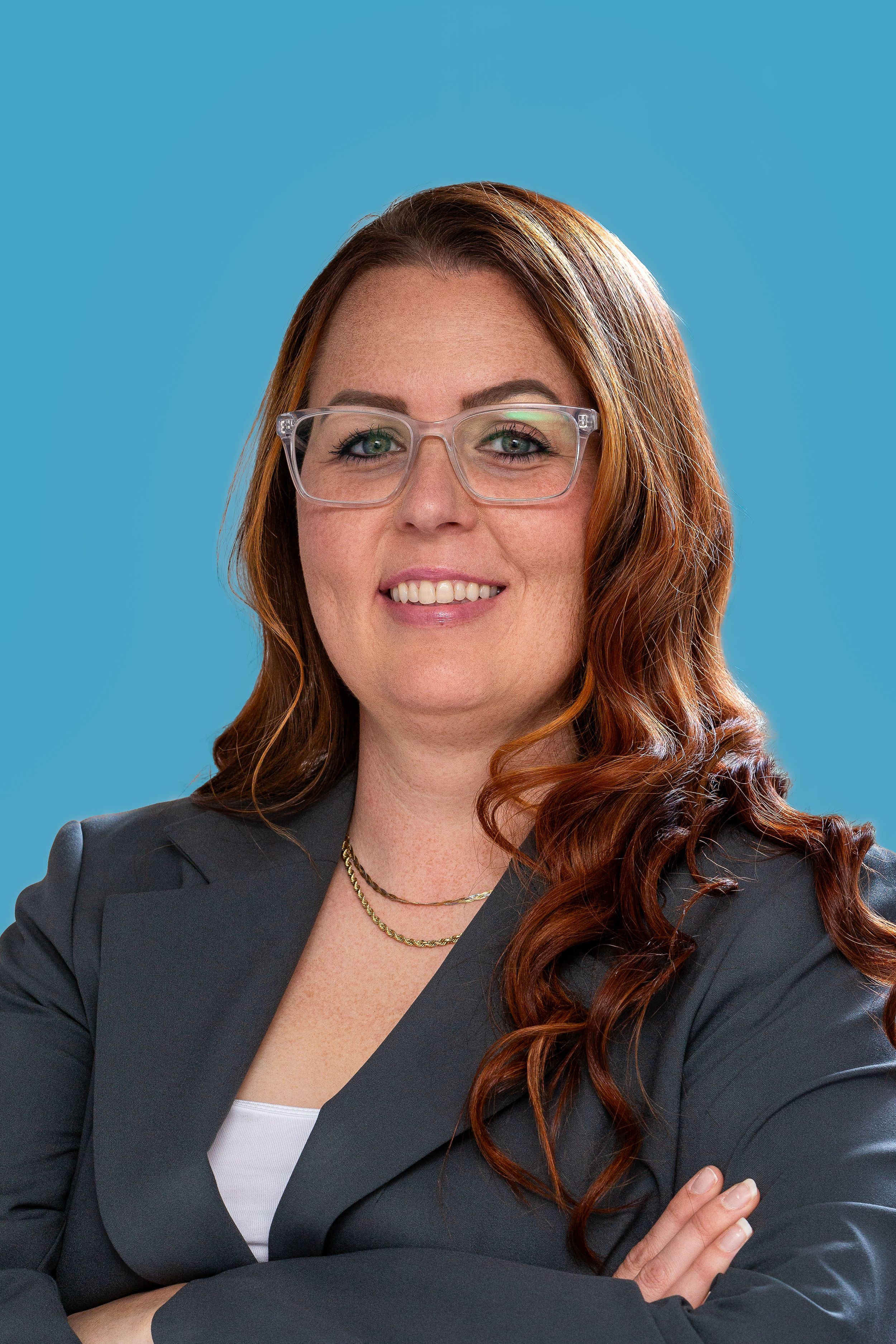 Professional headshot of person in gray blazer and glasses against blue background.