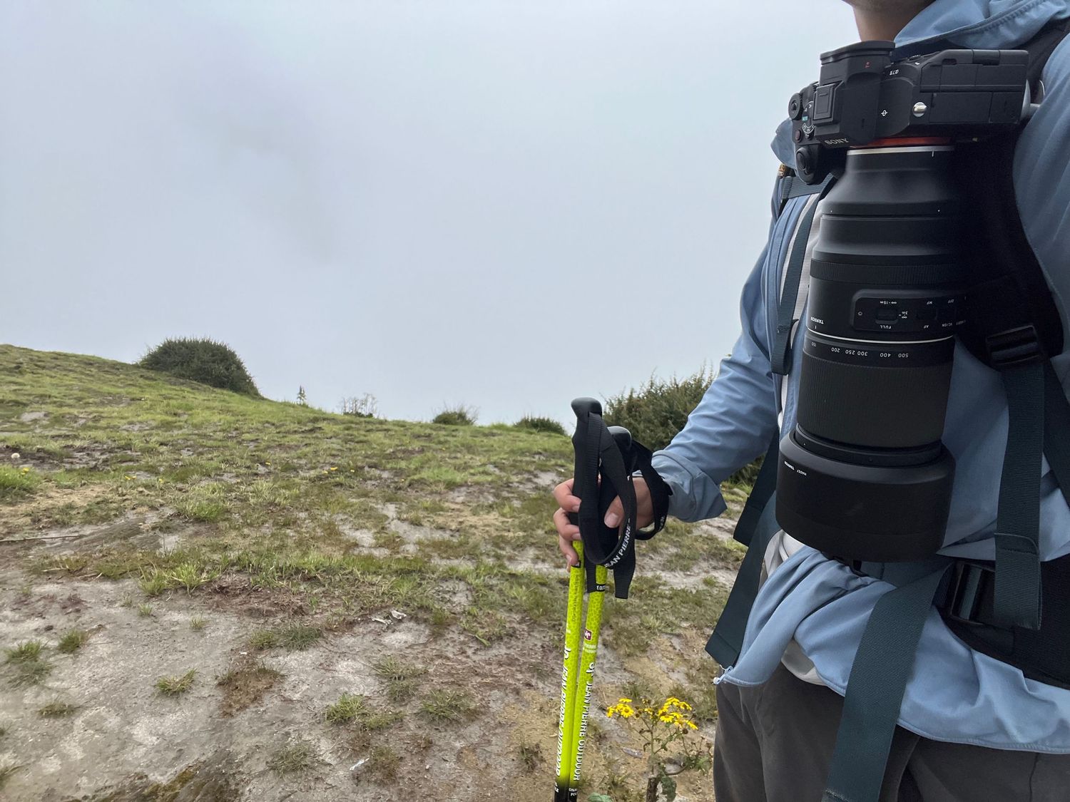 Hiking equipment and gear being adjusted on a mountain trail with cloudy background.