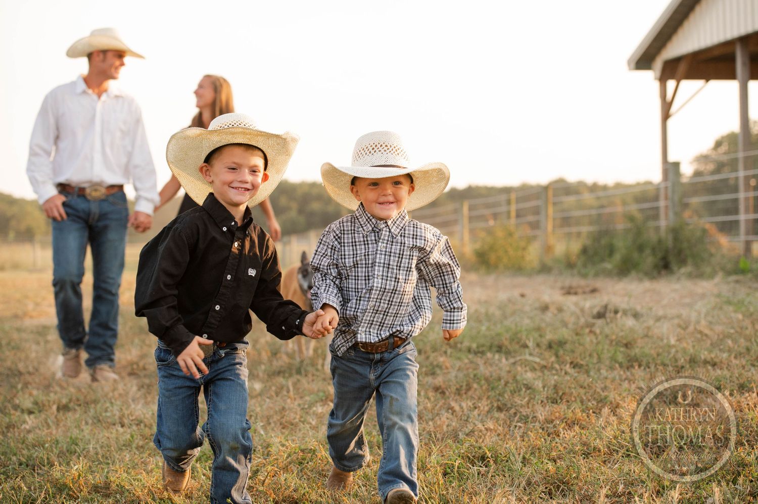 Two young cowboys run joyfully across a ranch field at sunset.