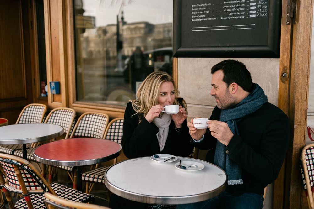 A couple enjoys coffee together at an outdoor Parisian cafe with traditional rattan chairs and bistro tables.