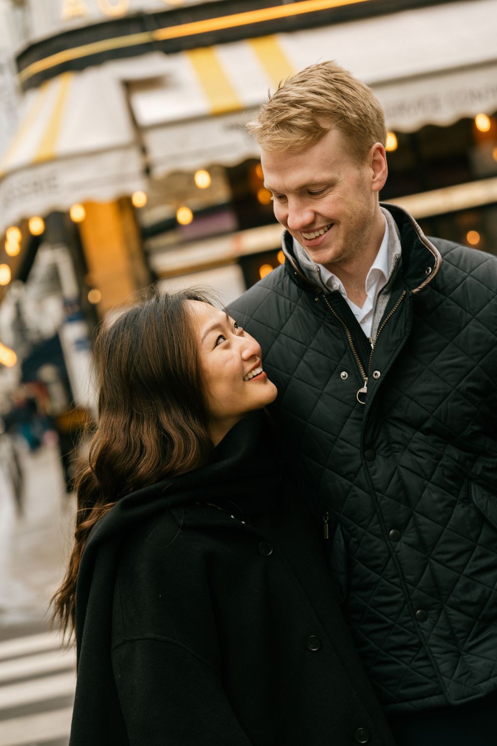 A joyful couple shares a loving moment together outdoors during evening hours wearing dark winter coats.