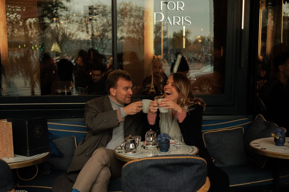 A couple shares an intimate moment at a cozy Paris cafe with wine glasses during twilight hours.