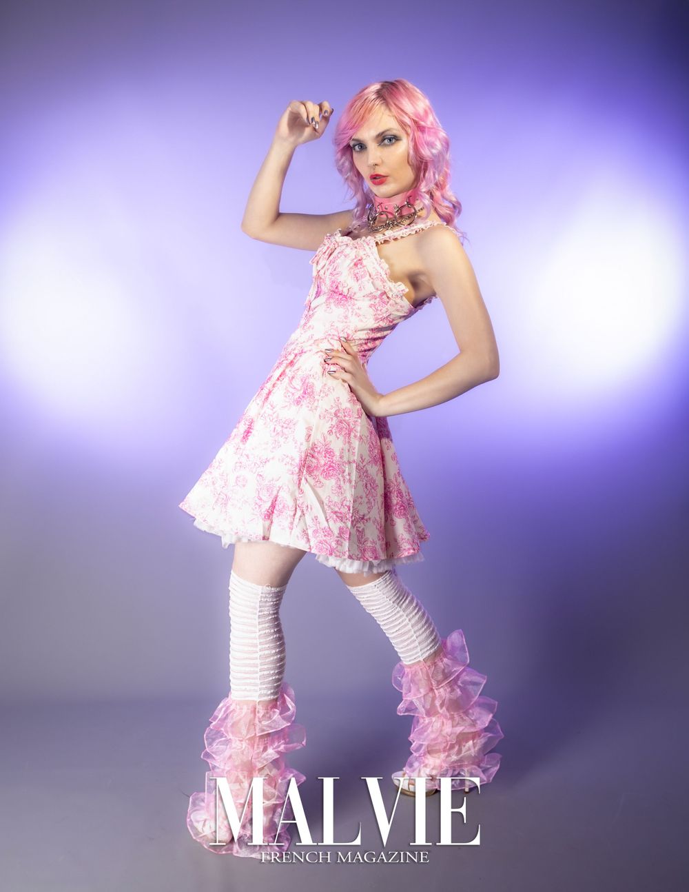 Fashion model in pink floral dress and matching legwear poses against purple background.