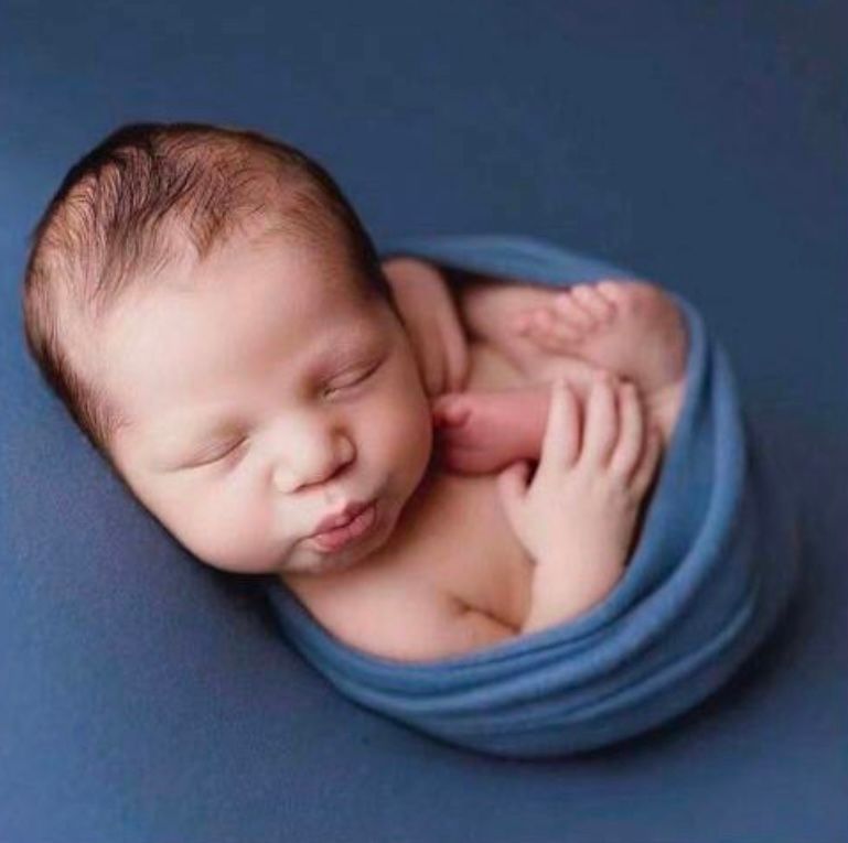 Sleeping newborn wrapped in soft blue fabric against navy backdrop.