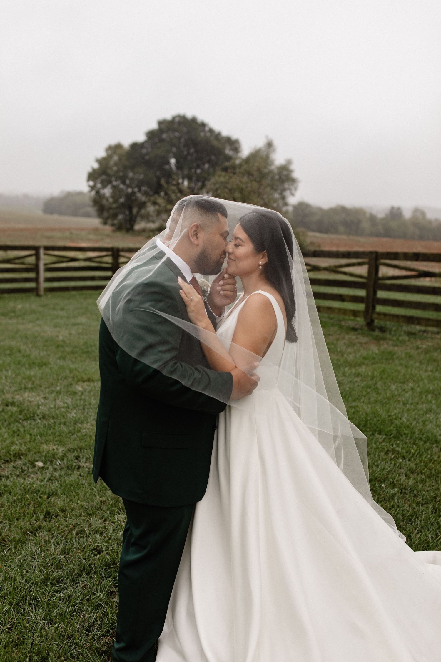 A couple embraces in an intimate moment on their wedding day with a rustic fence backdrop.