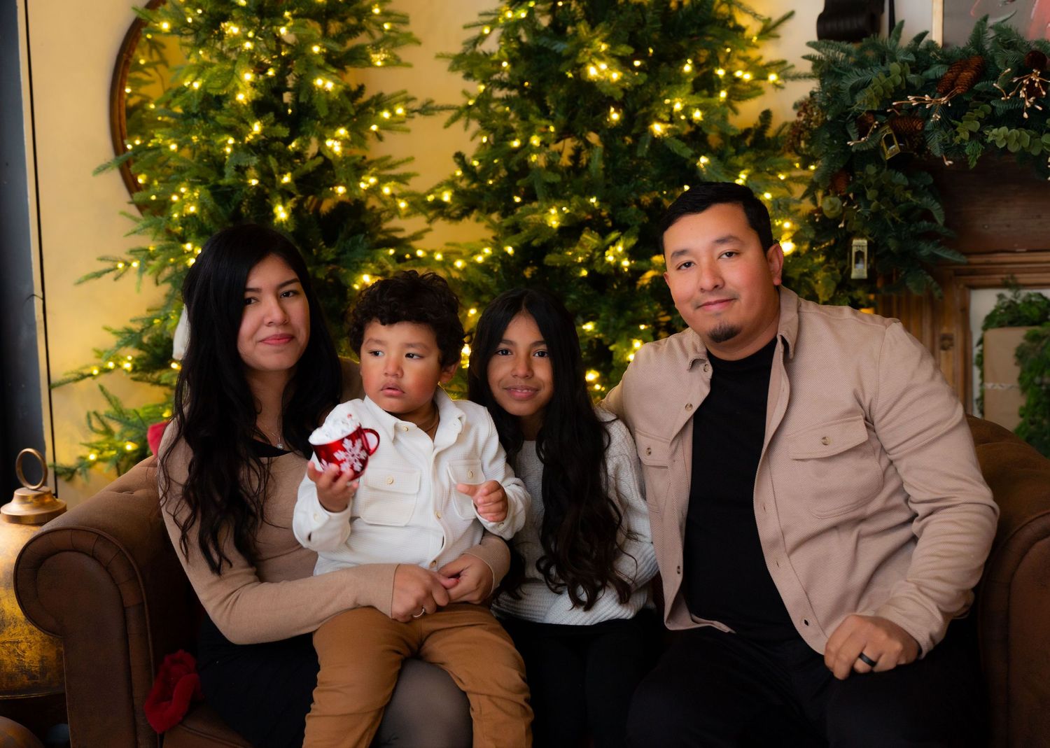Family of four posed on couch with Christmas tree and holiday decorations in background.