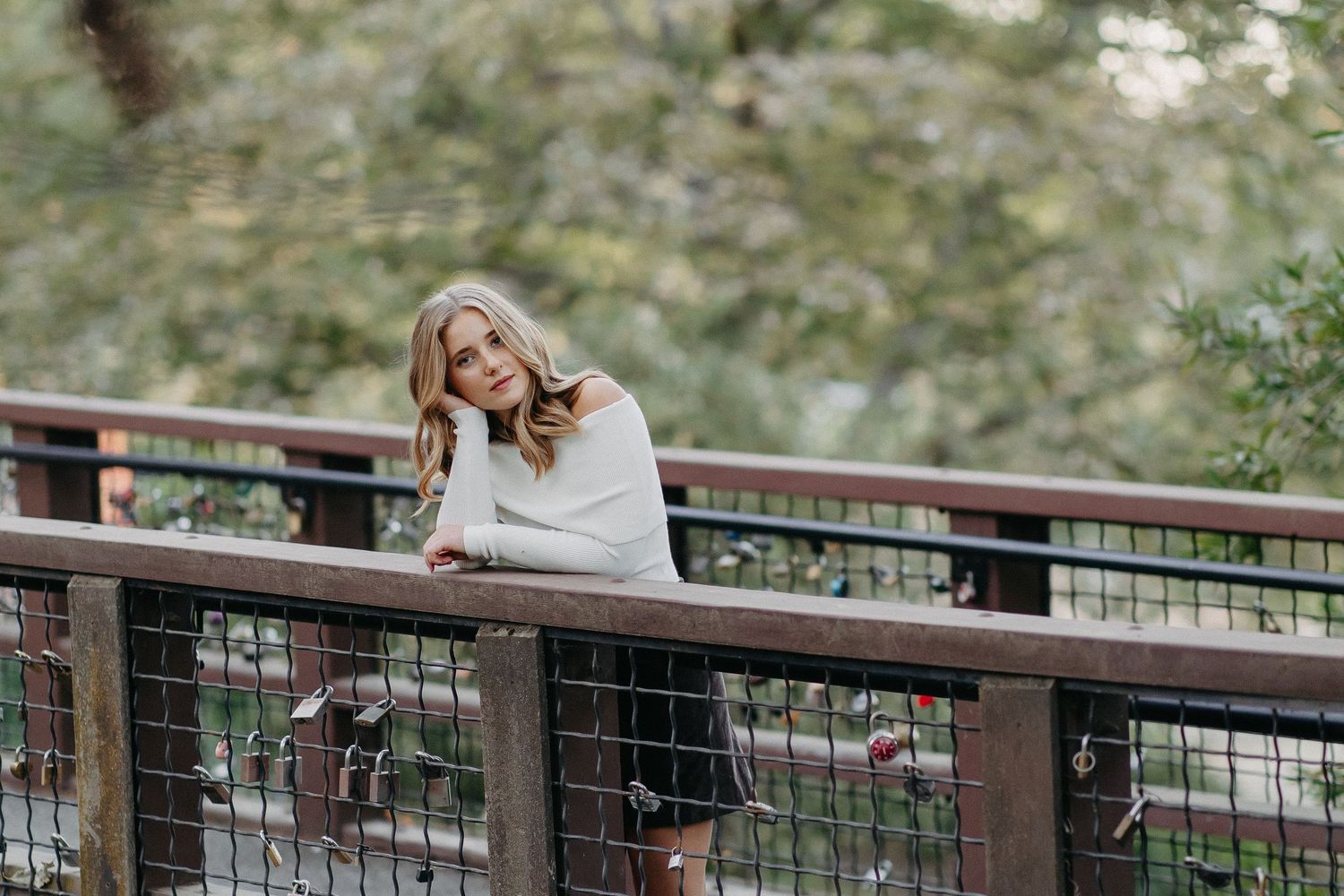 Person in white sweater leaning on wooden bridge railing in natural outdoor setting during autumn.
