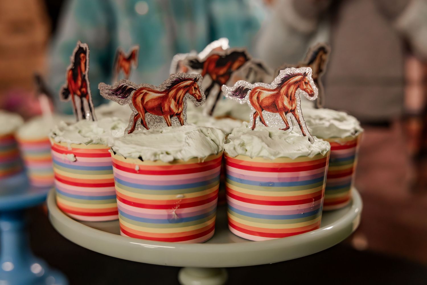 Colorful striped cupcakes decorated with horse-themed toppers featuring red and brown horses on white frosting.