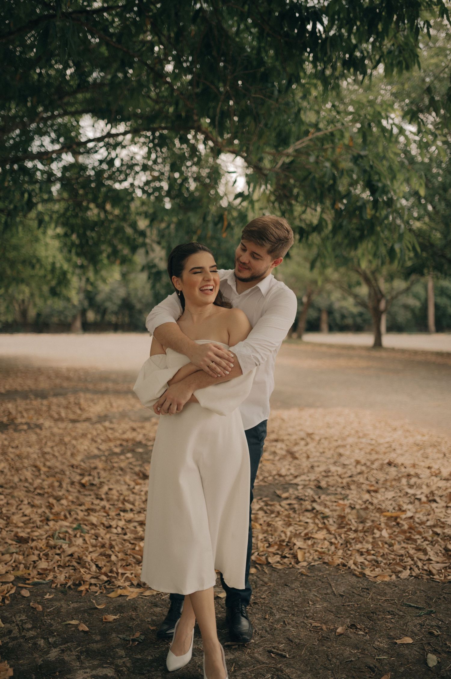 Joyful couple embracing on autumn path under tree canopy.