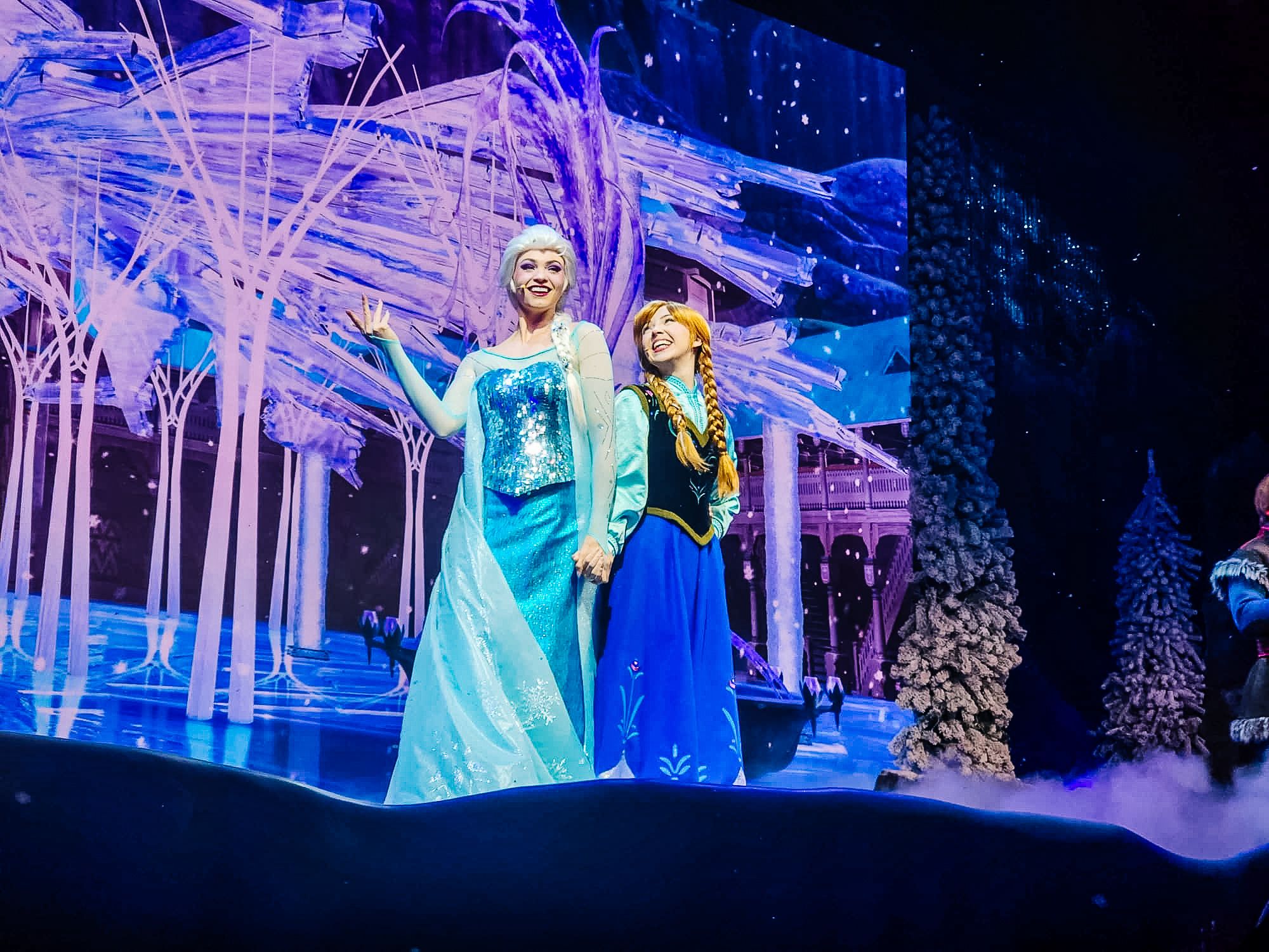 A colorful stage performance scene in blue and purple lighting with a winter theme and glowing trees.