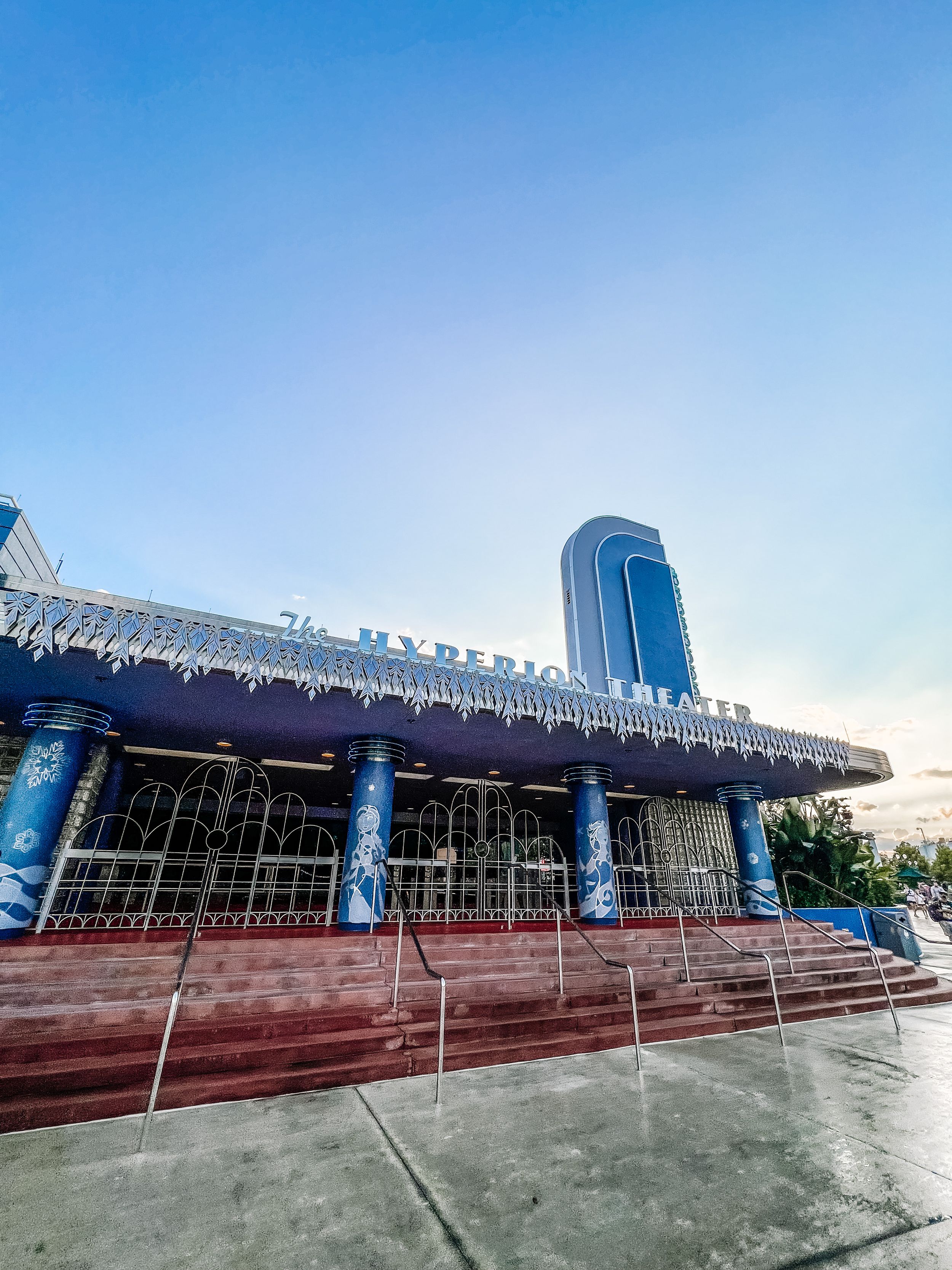Low angle view of a modern commercial building entrance with frosted glass windows and blue columns, topped by a decorative awning.