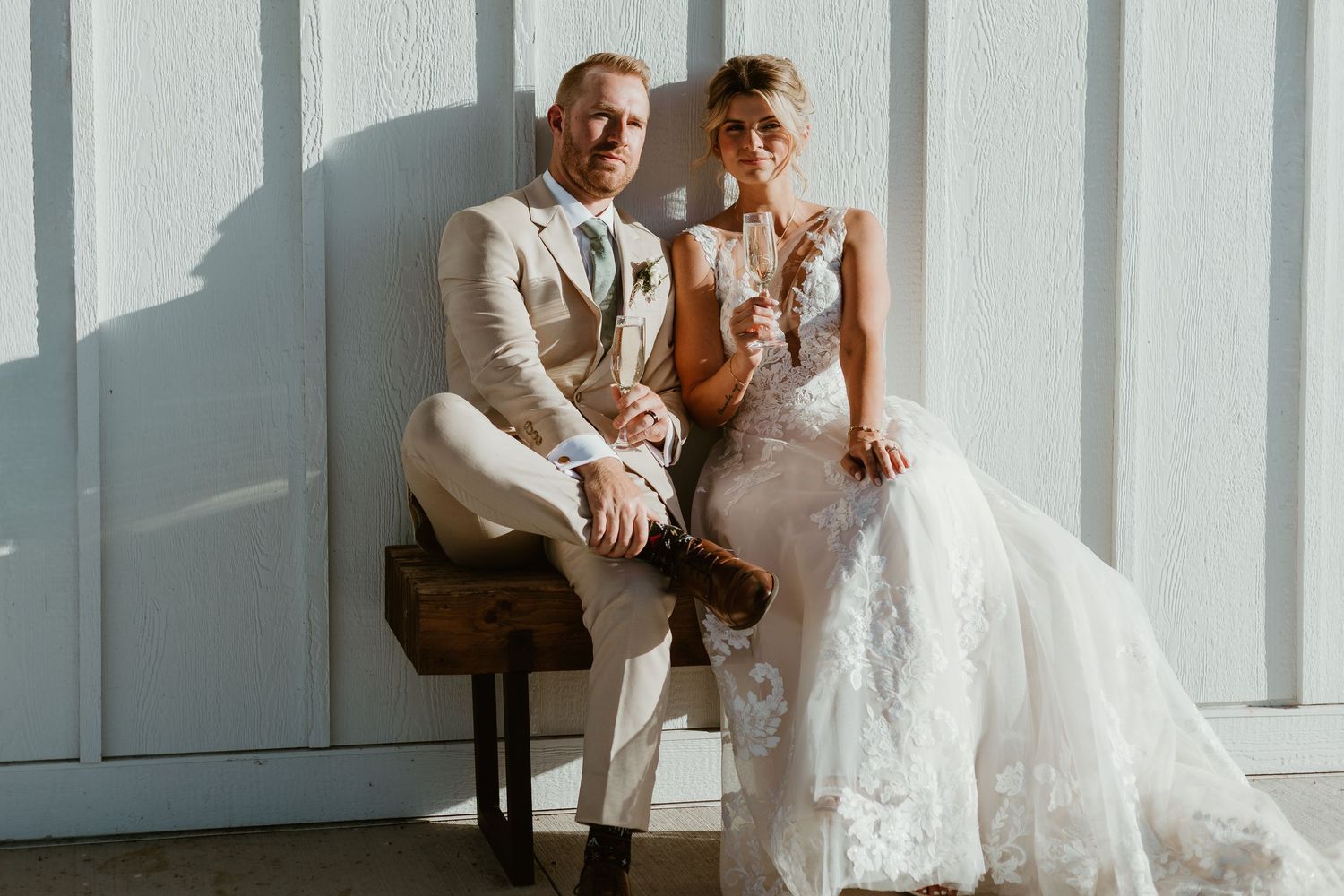 A romantic wedding photo in a forest setting with a flowing white dress and light gray suit against green foliage.