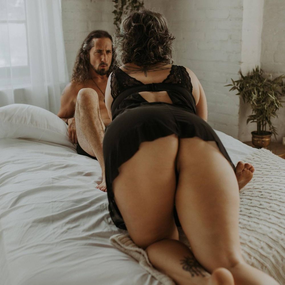 Sensual boudoir photo featuring a couple embracing in an intimate moment on a white bed with natural window lighting.