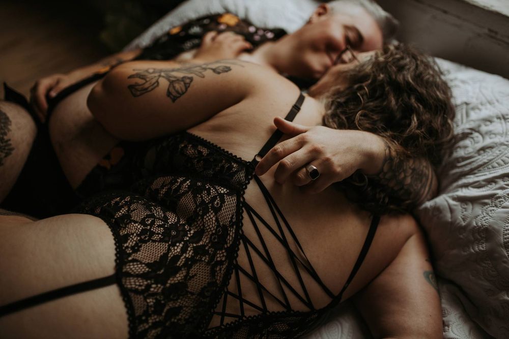Two women in black lace lingerie lying together on a bed in an intimate boudoir photography session.