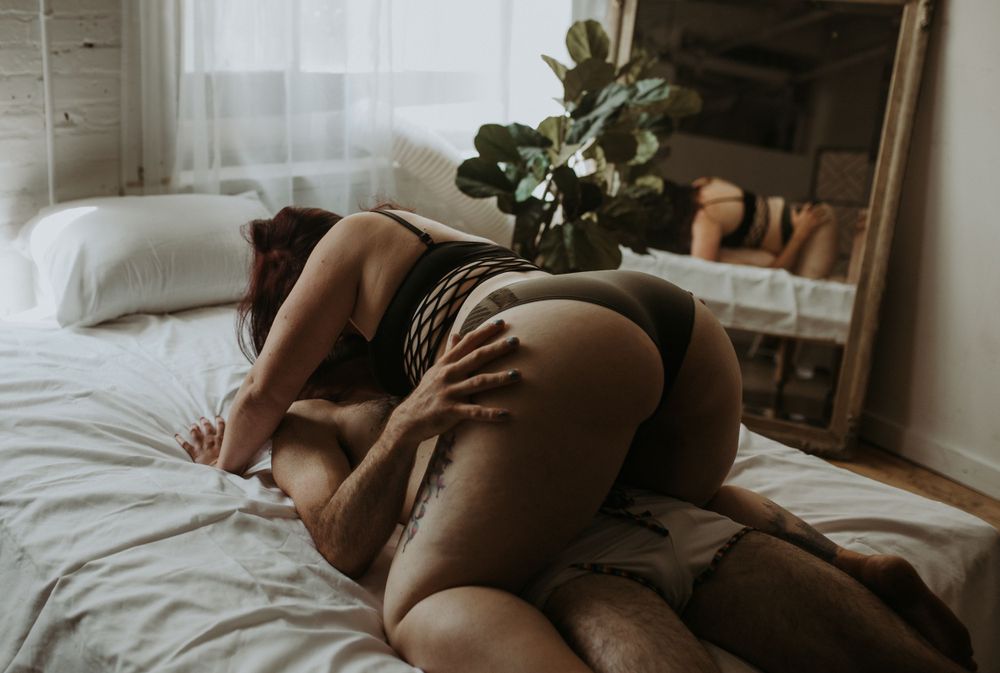 A sensual boudoir photograph showcasing an intimate pose of a couple on a bed in soft natural window light.