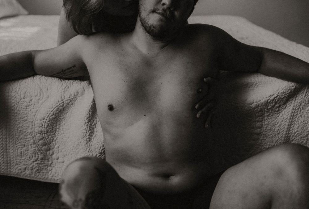 Black and white artistic photograph of a shirtless torso and limbs reclining on white fabric.