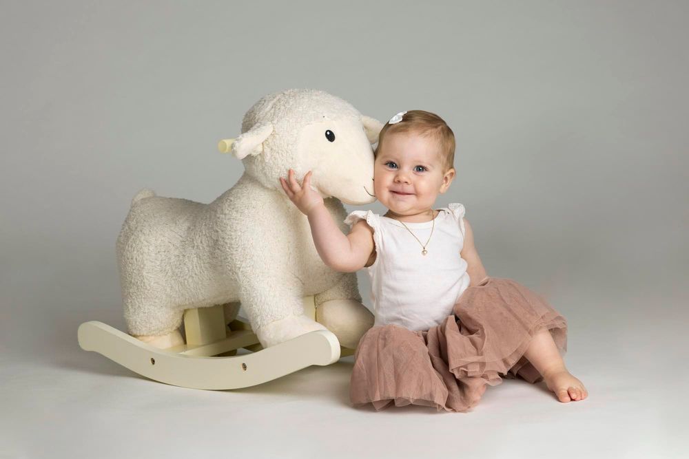 1-åring sittende i fotostudio som koser med et gyngelam hos barnefotograf i Lyngdal