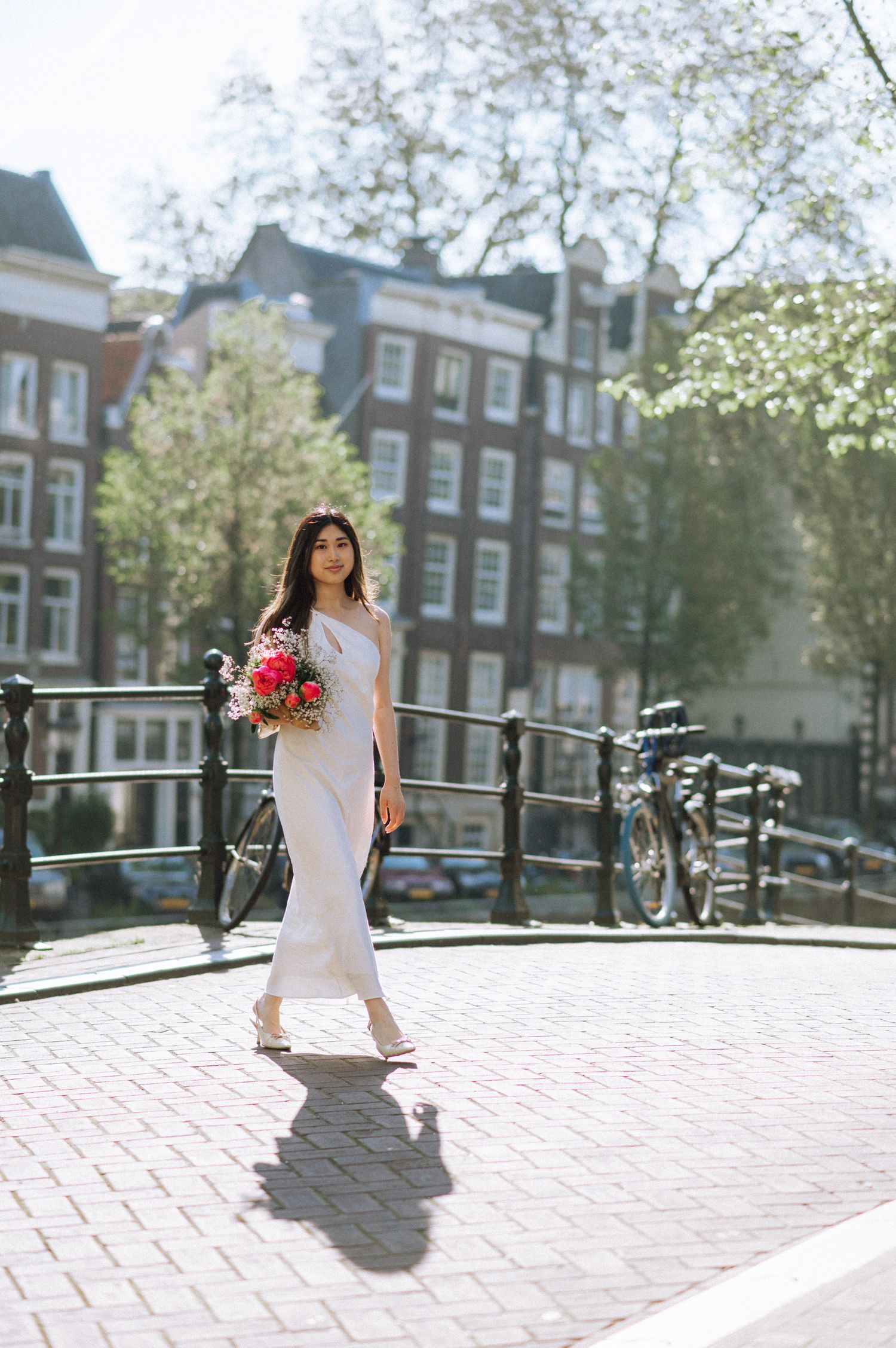 Woman crossing a canal bridge in Amsterdam. A beautiful lady in a white dress holding a bouquet.