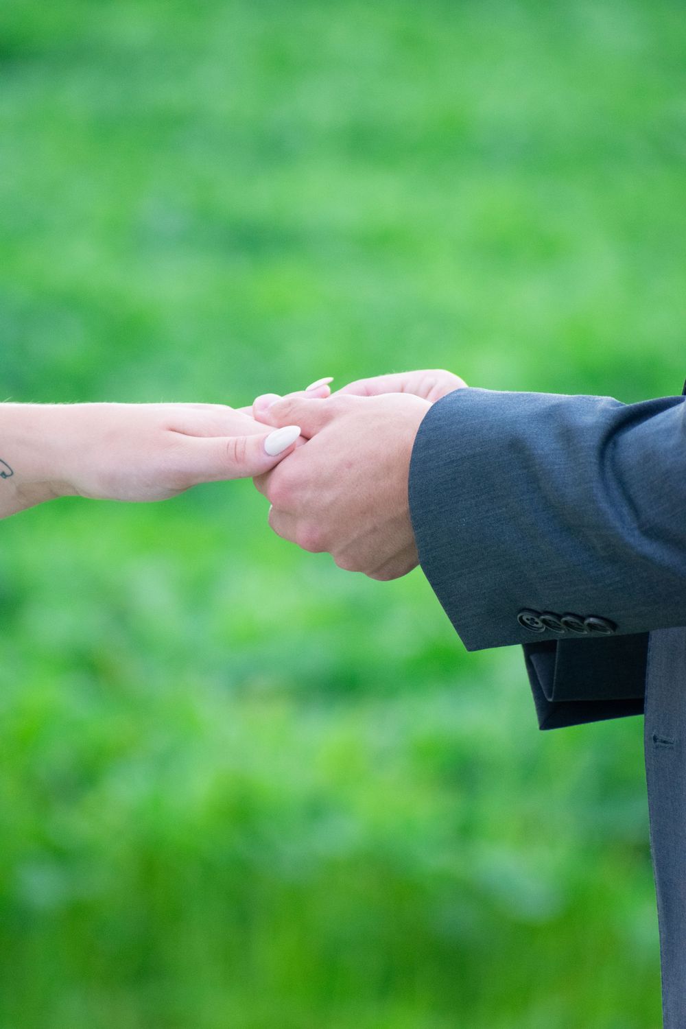 Two hands clasp together in a tender gesture against a blurred green natural background outdoors.