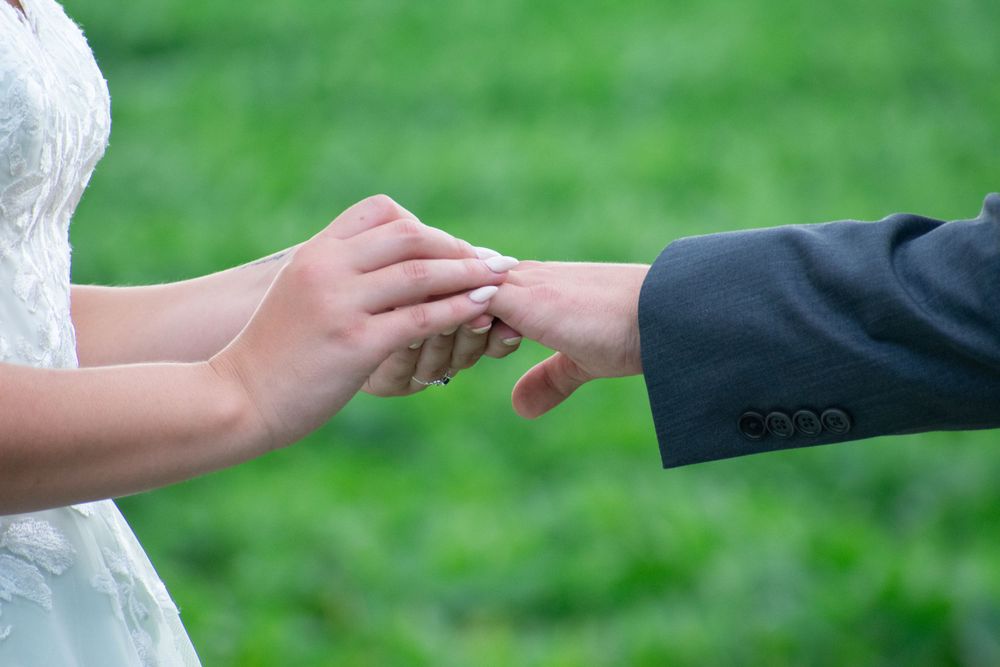 Close-up of hands exchanging wedding rings during outdoor ceremony with green grass background.