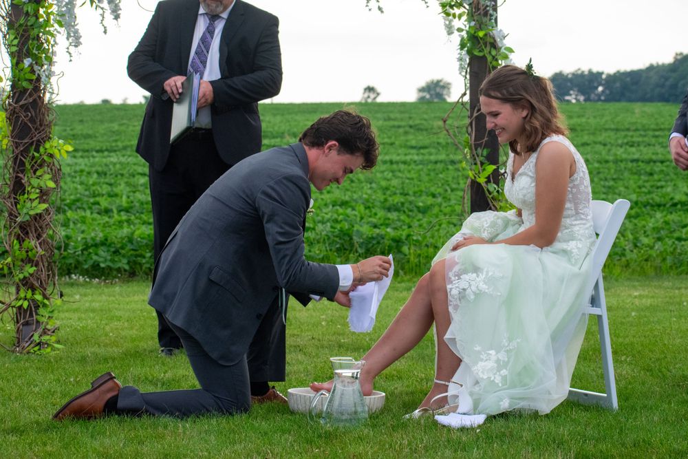 A romantic wedding ceremony moment takes place outdoors on a lush green lawn with white decor and spring trees.