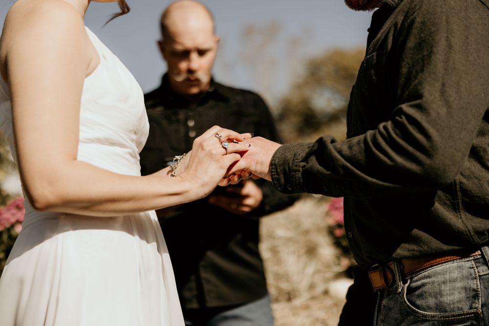 Close-up of hands exchanging rings during an outdoor wedding ceremony.