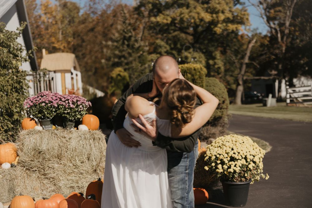 Fall decorative display with hay bales, pumpkins, and mums outside a home on a sunny autumn day.