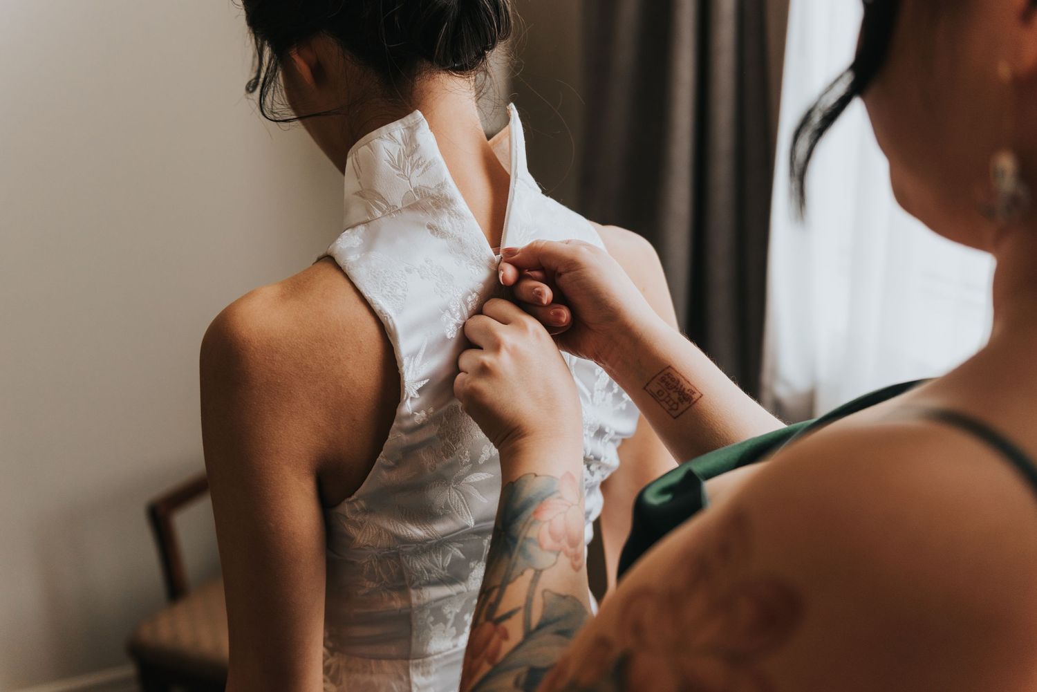 Someone helps button up a delicate white lace wedding dress during bridal preparation.