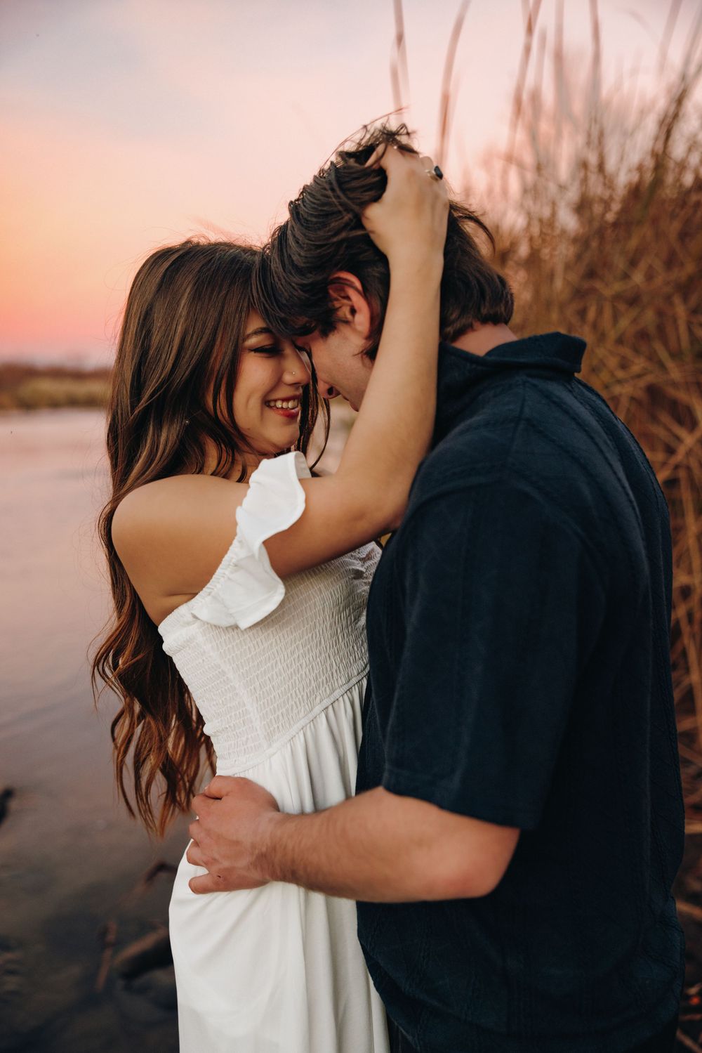 A couple shares an intimate embrace at sunset near tall grass at the Salt River with warm golden lighting.