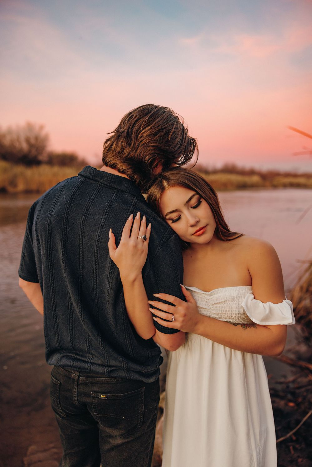 A couple shares an intimate embrace at the Salt River during sunset with soft pink skies in the background.