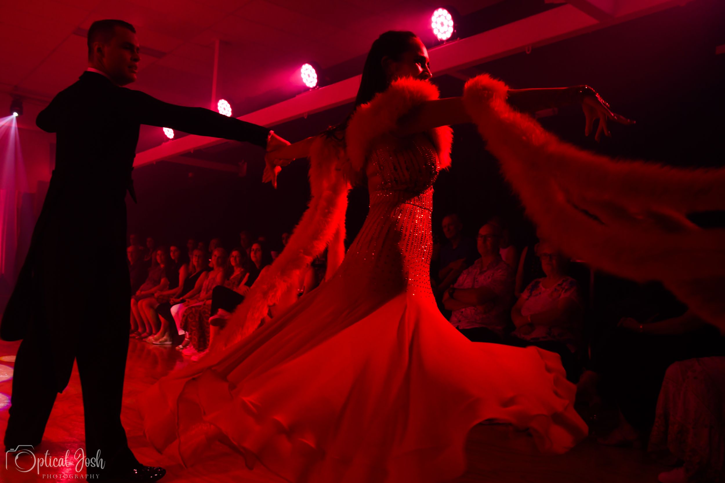 A couple dancing in dramatic red lighting while flowing fabric swirls around them during a ballroom performance.
