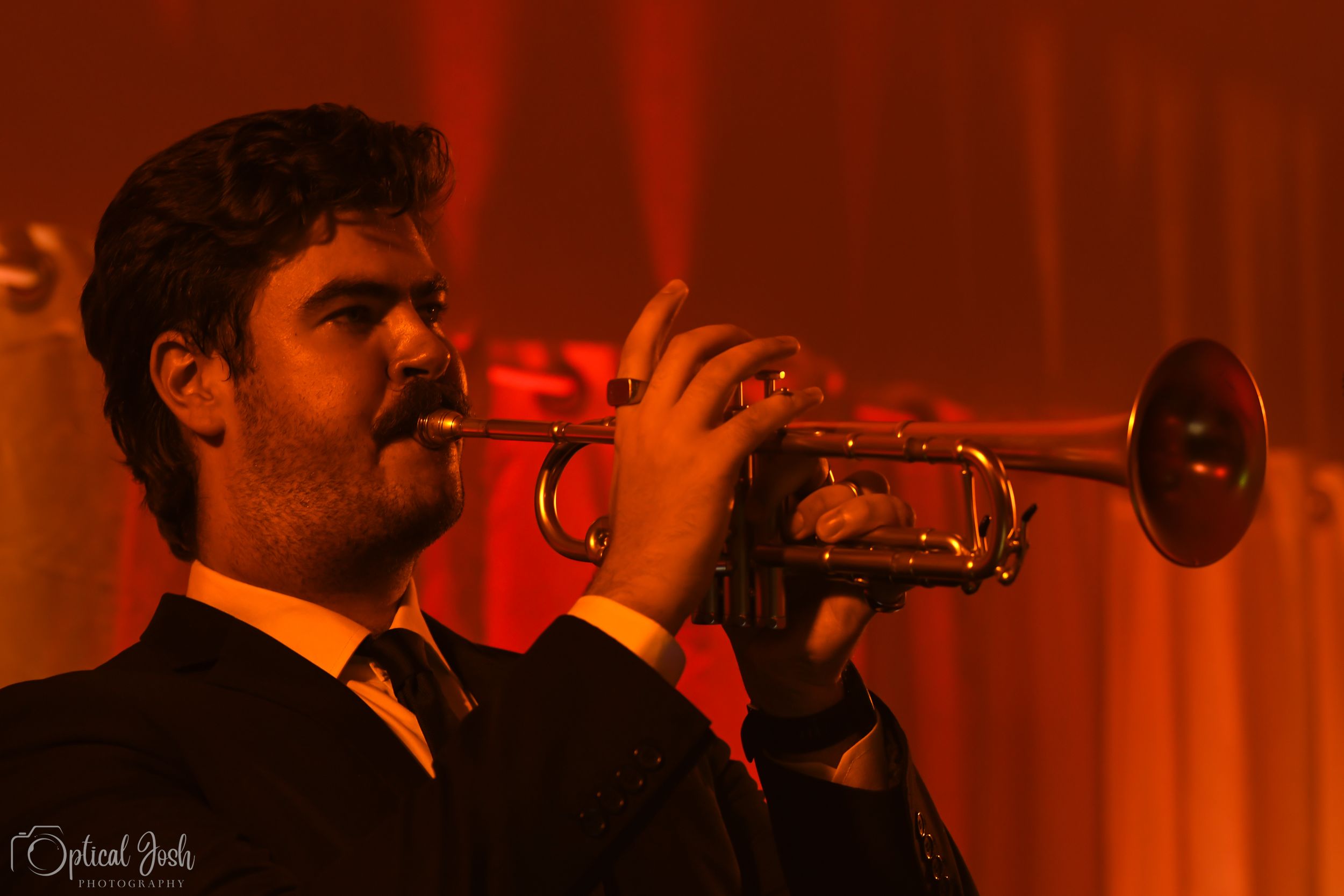 A musician plays trumpet on stage bathed in warm red lighting during a performance.