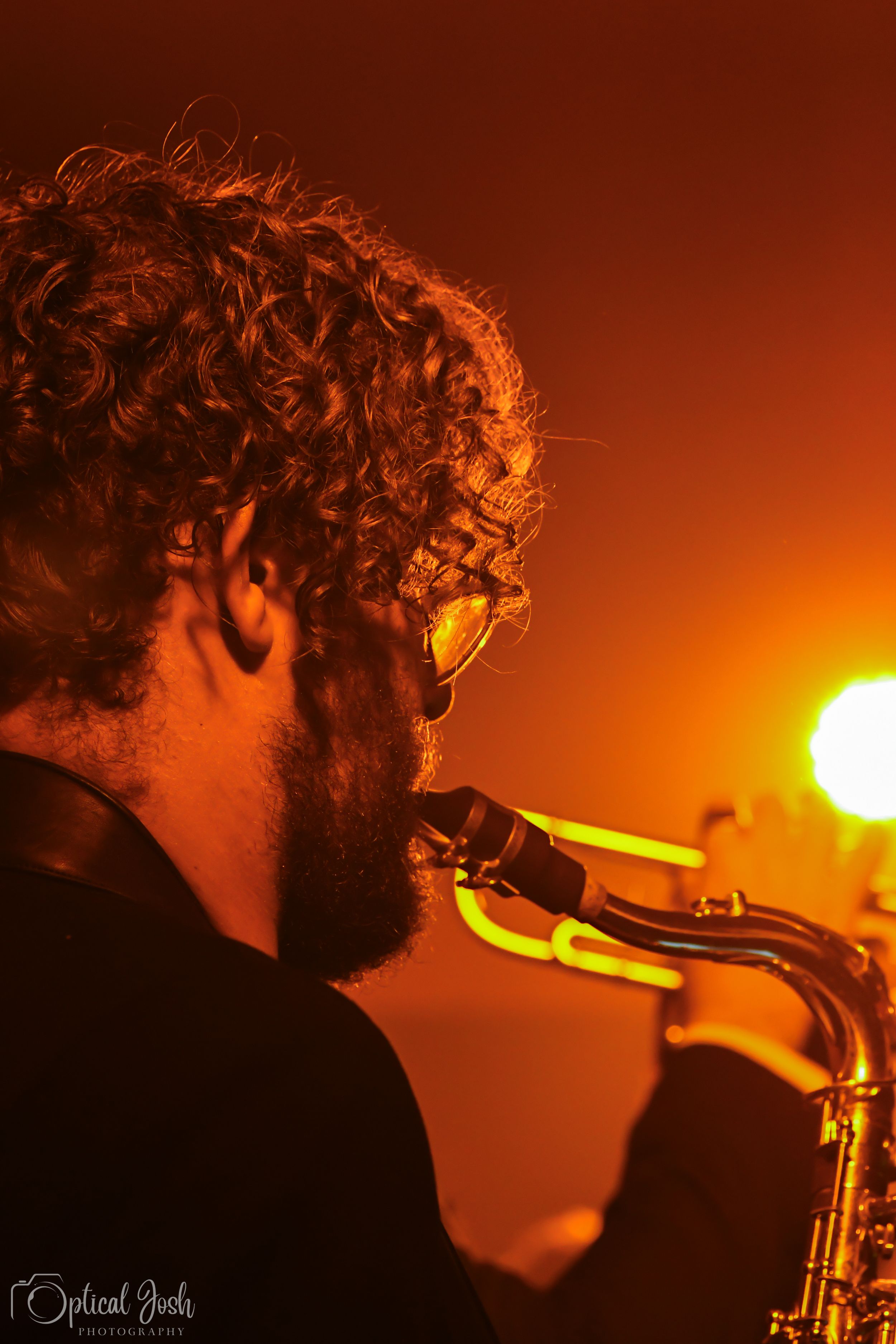 Silhouetted musician plays saxophone against warm orange stage lighting during dramatic performance.