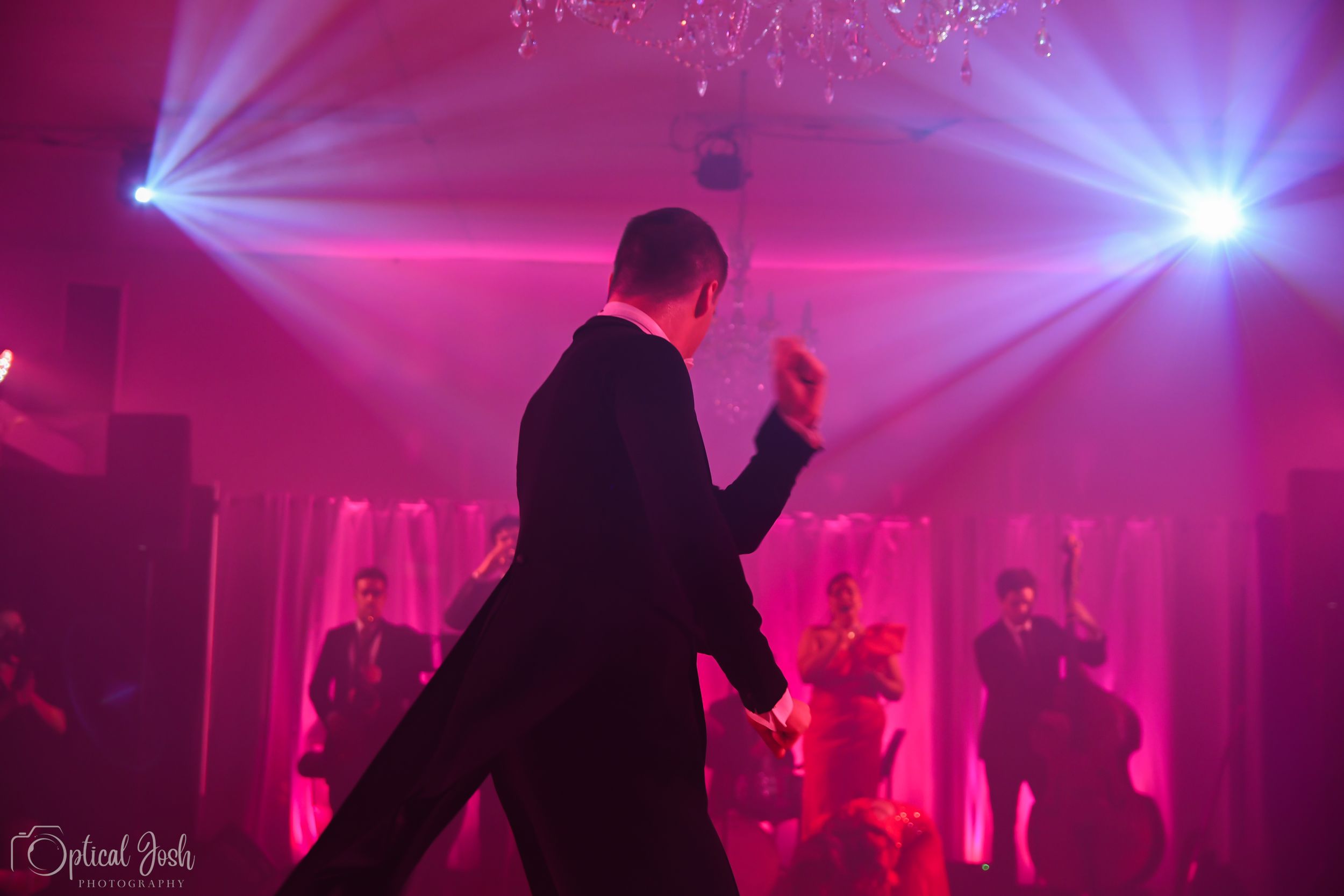 A silhouetted performer dances on stage with dramatic pink and blue spotlights creating an atmospheric scene.
