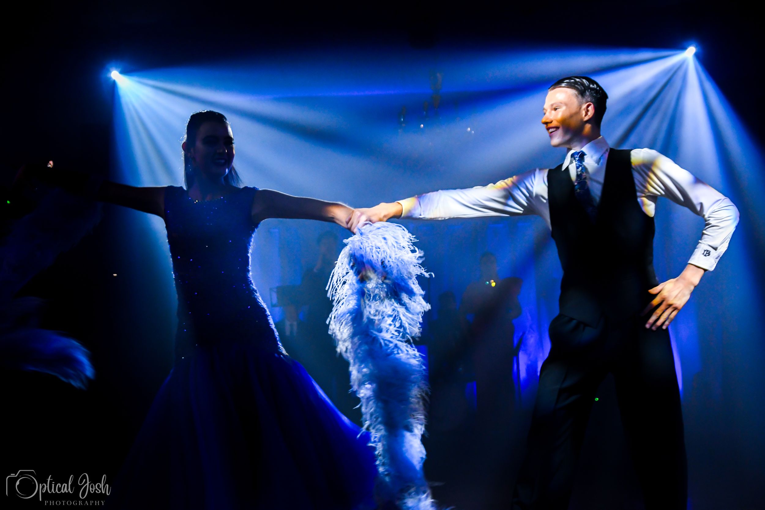 A dramatic performance scene with blue stage lighting casting shadows as two people dance expressively on stage.