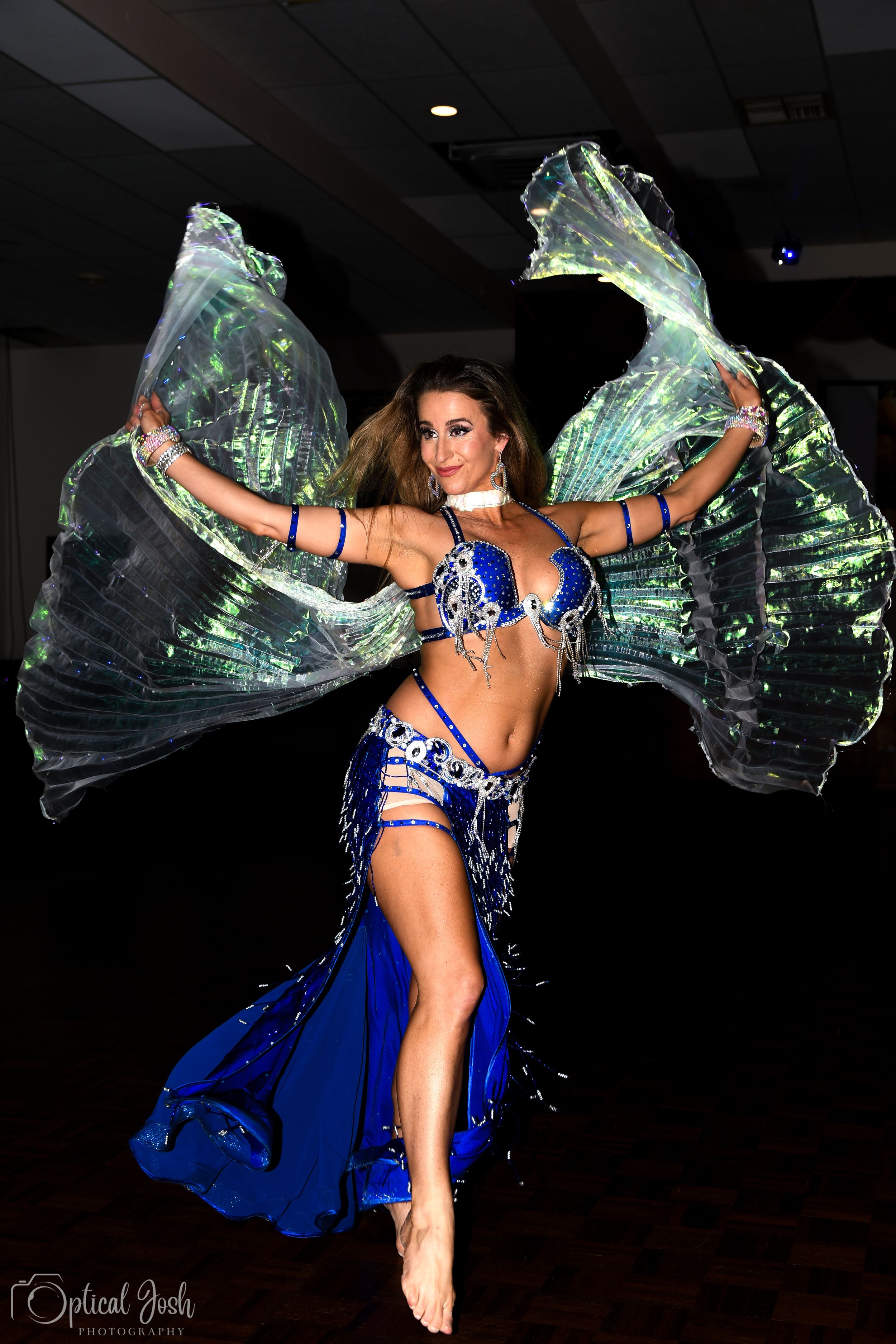 A belly dancer performs with flowing veils in a sparkly blue costume during a dynamic dance performance.