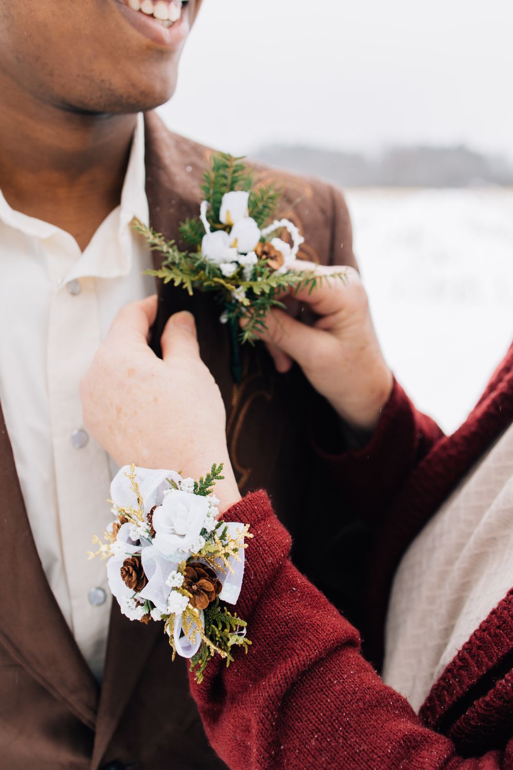 White floral boutonniere being pinned to a brown suit jacket.