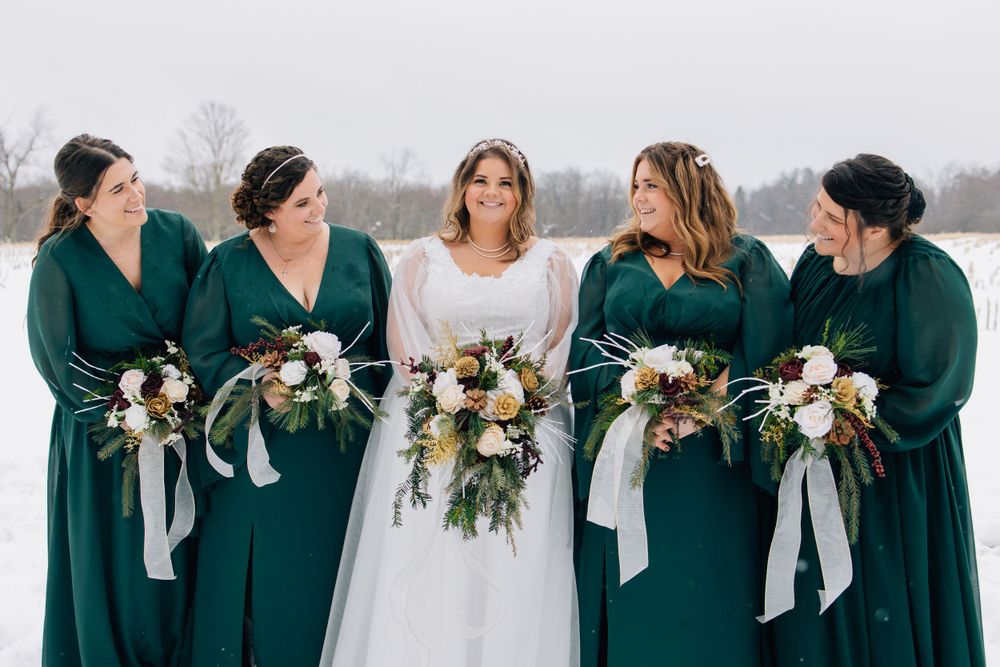 Wedding party of bridesmaids in emerald dresses with bride in white holding winter bouquets.