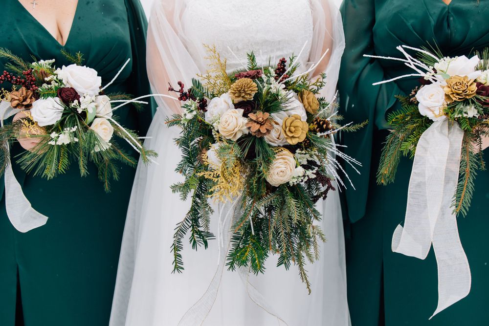 Close-up of wedding bouquets featuring roses, evergreens and cream ribbons against emerald dresses.
