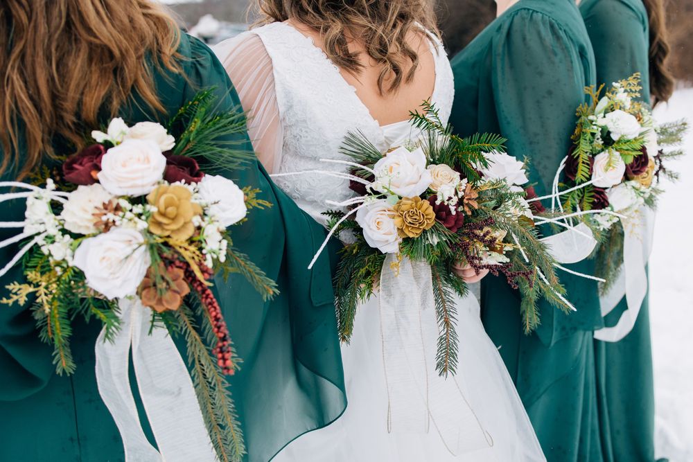 Bridesmaids in emerald green dresses hold elegant bouquets of white and burgundy flowers with greenery.