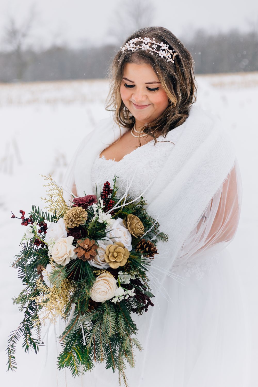 A winter bride holds a stunning bouquet of roses and evergreens while wearing a crystal headpiece.