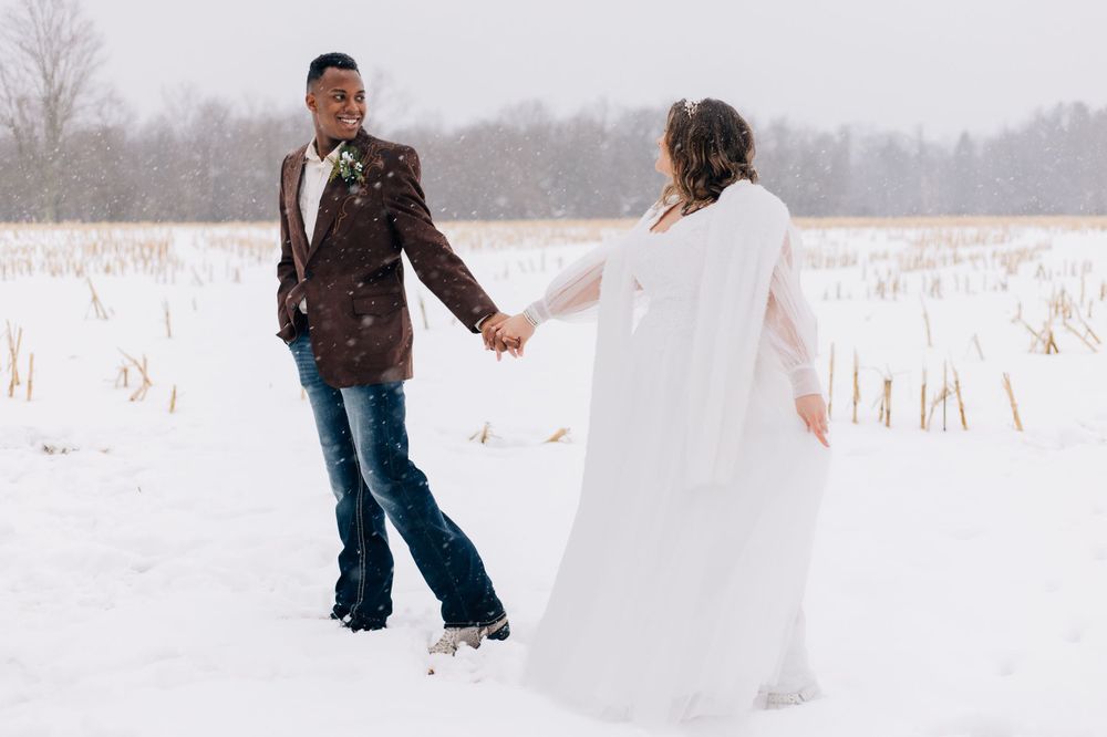 Wedding couple walking hand in hand through a snow-covered field on their winter wedding day.